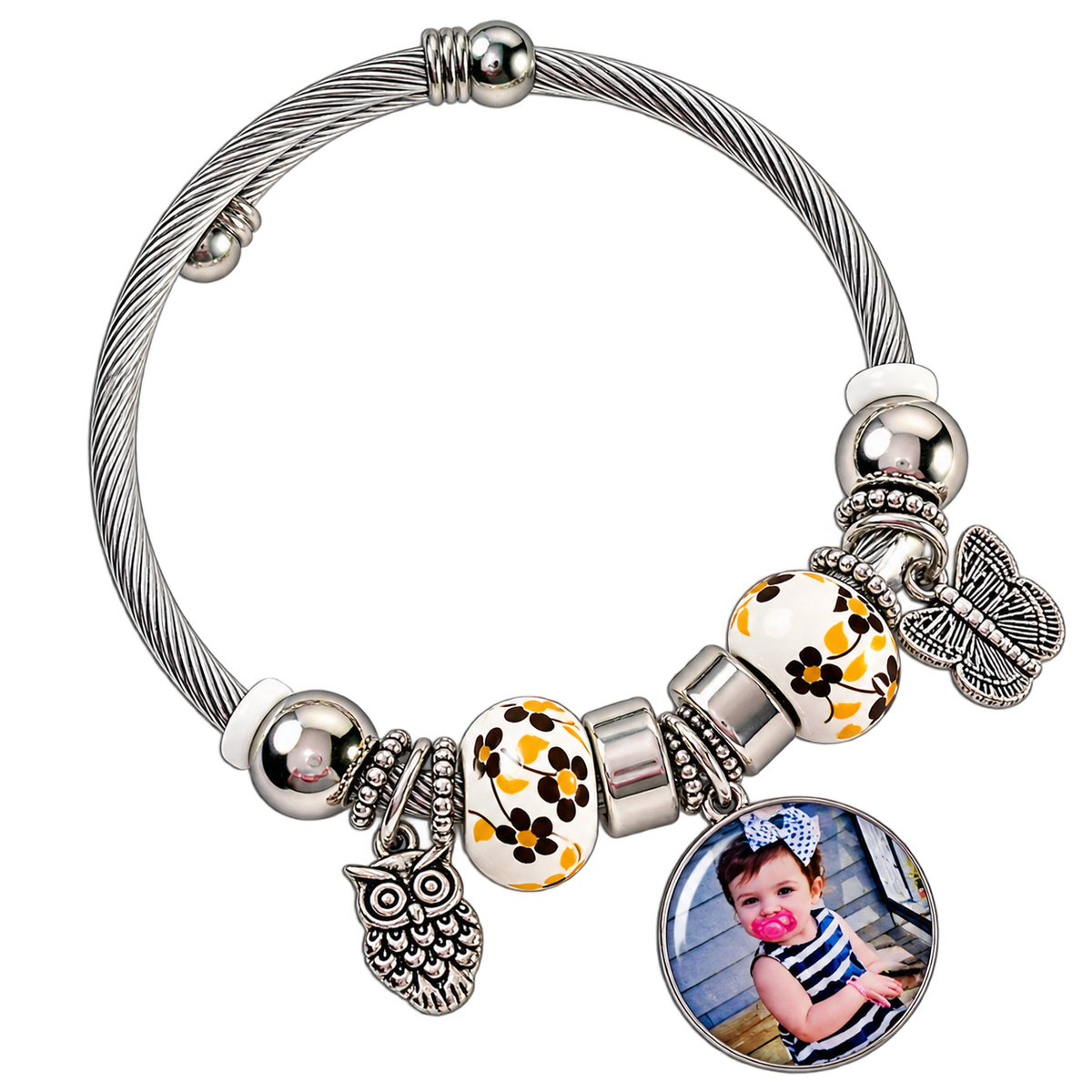 Angled view of A Memory to Wear photo bracelet with a round child portrait charm, floral beads, and silver-tone owl and butterfly charms.