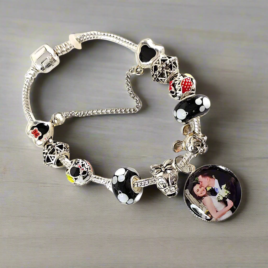 Angled view of Enchanted Memories photo charm bracelet on a gray surface, showing decorative mouse-themed beads and a silver-tone safety chain.