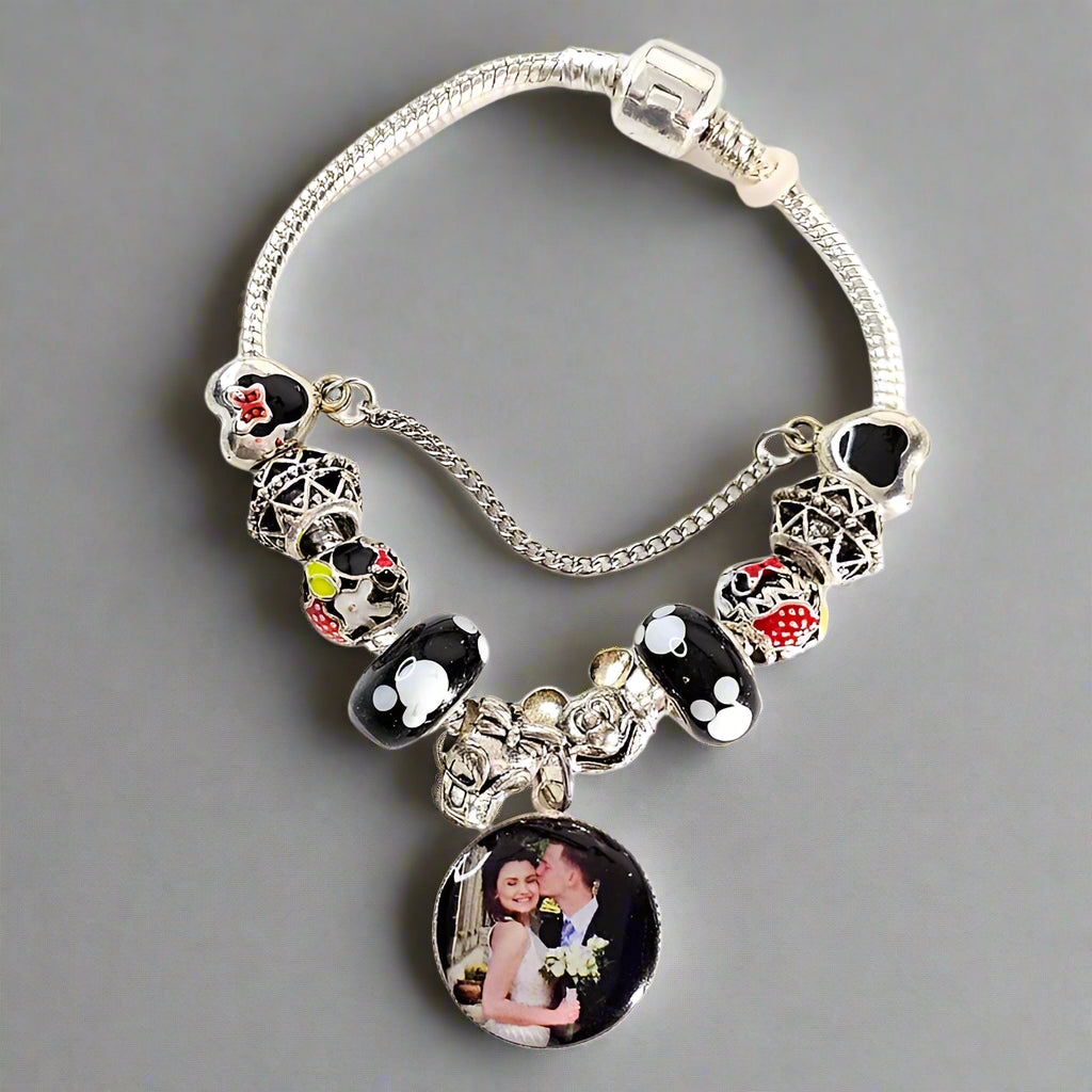 Enchanted Memories bracelet displayed on gray with a round couple photo charm, black and white beads, red accents, and silver-tone safety chain.