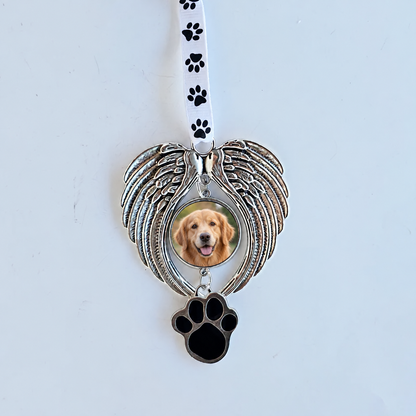 Silver-tone angel wing pet memorial ornament with a golden retriever photo, black paw-print charm, and white paw-print ribbon against a pale background.