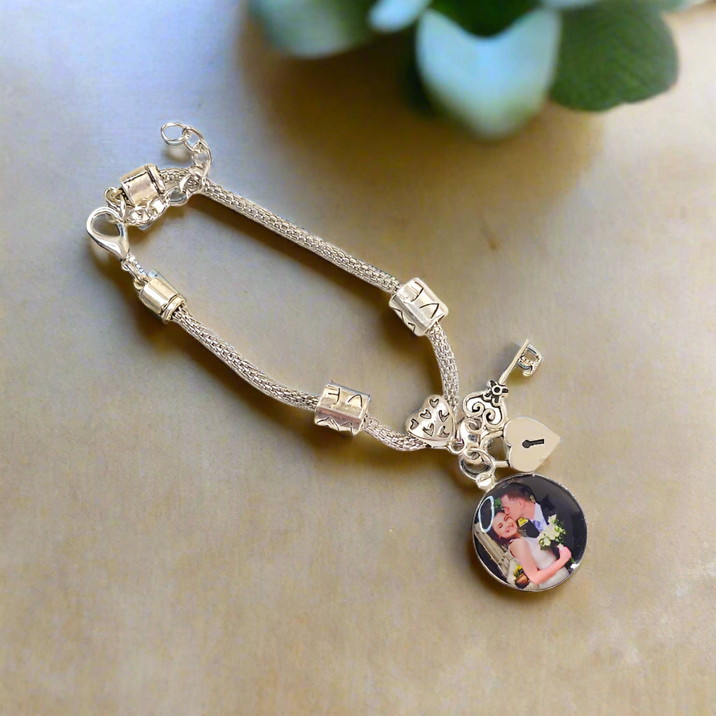 Angled view of Keys to My Heart photo bracelet on a tabletop, showing a couple’s portrait, silver-tone beads, and heart lock and key charms.