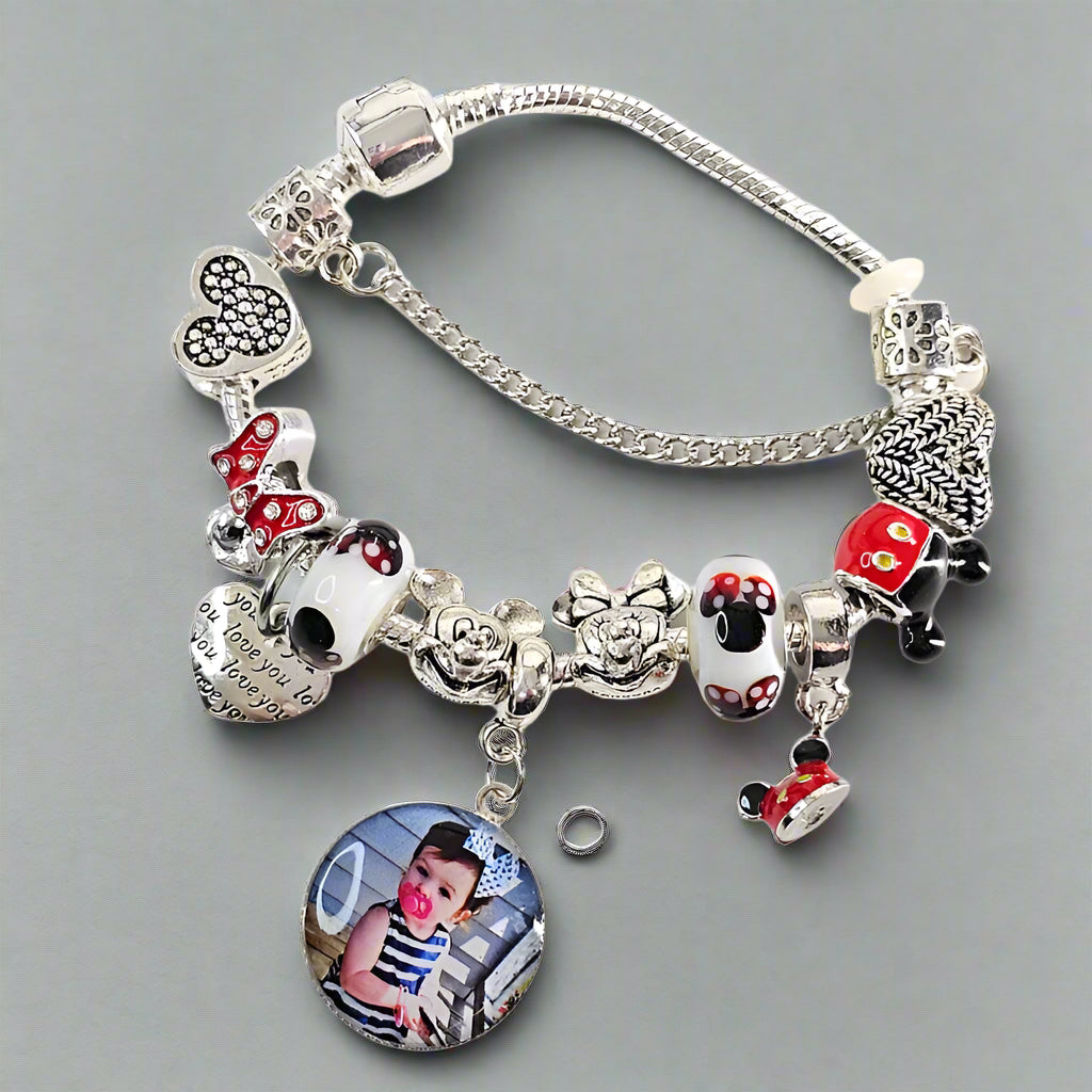 Magical Memories photo charm bracelet on a gray surface, showing mouse-themed beads, dangling charms, and a silver-tone safety chain.