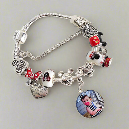 Angled view of Magical Memories personalized bracelet with a child’s portrait charm, red bow accents, and black and white mouse-themed beads.