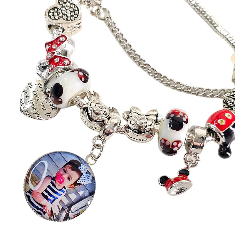 Close-up of Magical Memories bracelet showing a round child photo charm, red bow bead, mouse-themed beads, and dangling silver-tone accents.