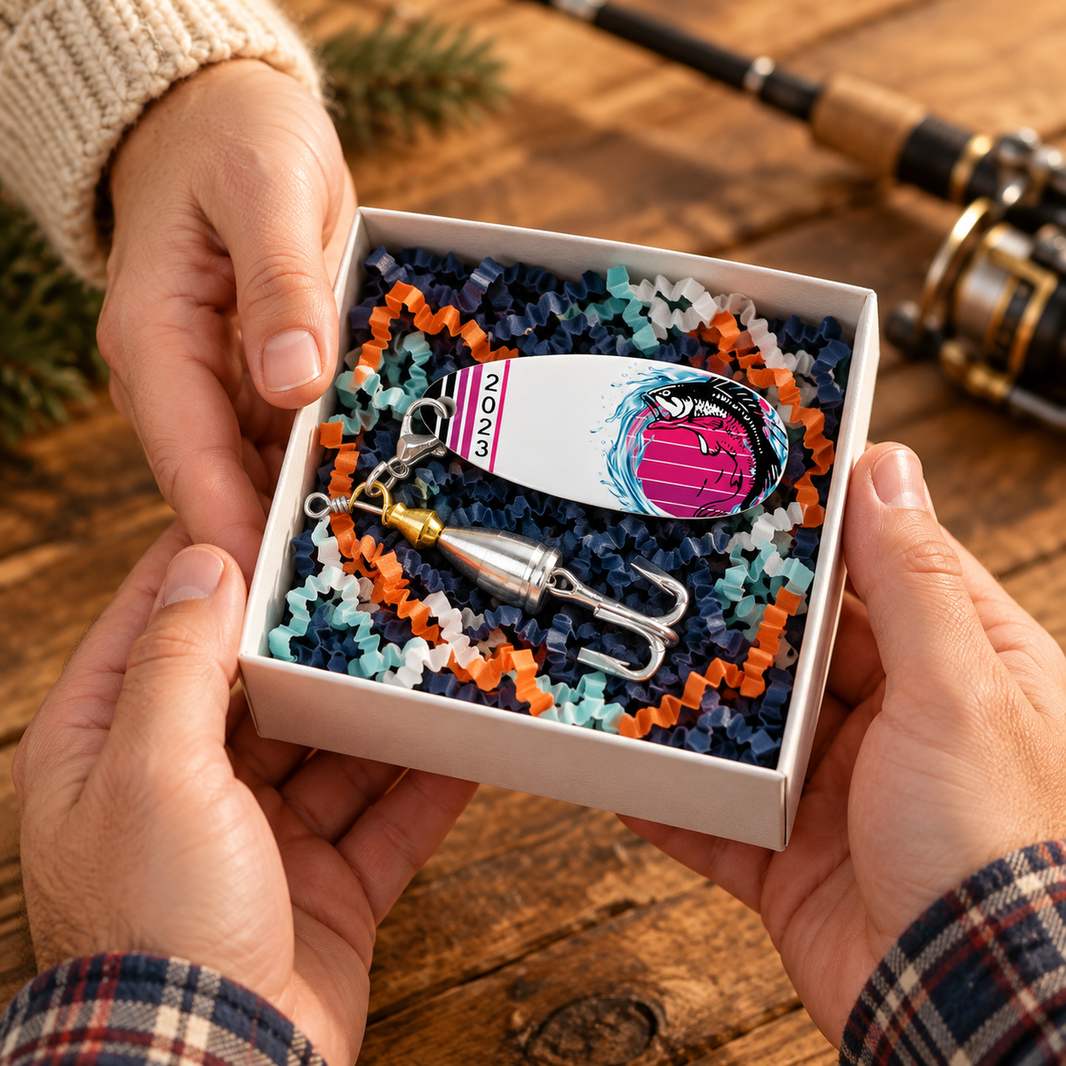 Hands presenting a Purple Sunset Leaper fishing lure in an open white gift box with navy, orange, teal, and white crinkle paper.