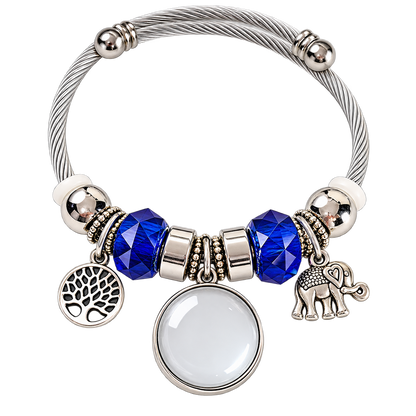 Rooted in Memories bracelet before personalization, featuring a blank round photo charm, blue faceted beads, and tree of life and elephant charms.