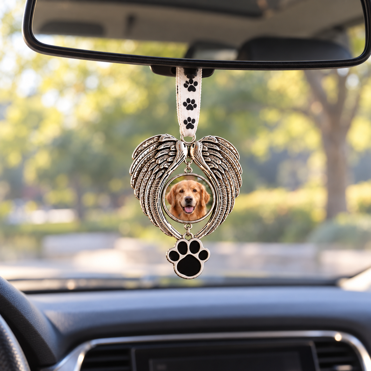 Golden retriever photo in a silver-tone angel wing pet memorial ornament hanging by a paw-print ribbon from a car rearview mirror.