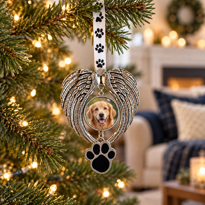 Silver-tone angel wing ornament with a golden retriever photo and black paw charm hanging from a paw-print ribbon on a lit Christmas tree.