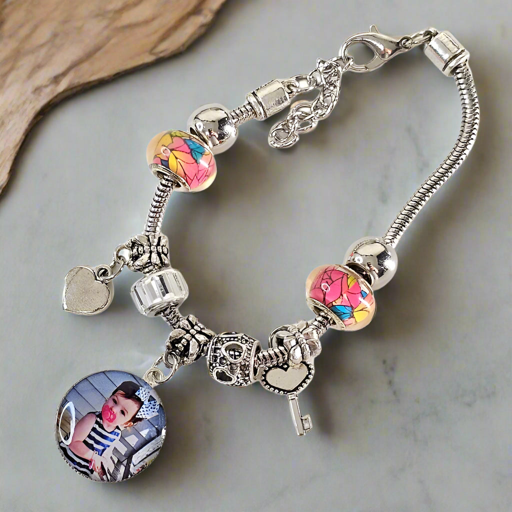 Angled view of The Key to My Heart bracelet on a gray surface, showing a child’s photo charm, colorful beads, and silver-tone heart and key accents.