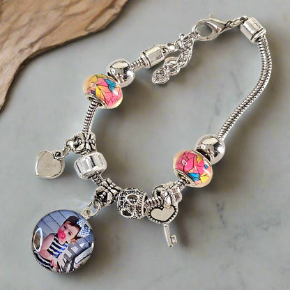 Angled view of The Key to My Heart bracelet on a gray surface, showing a child’s photo charm, colorful beads, and silver-tone heart and key accents.