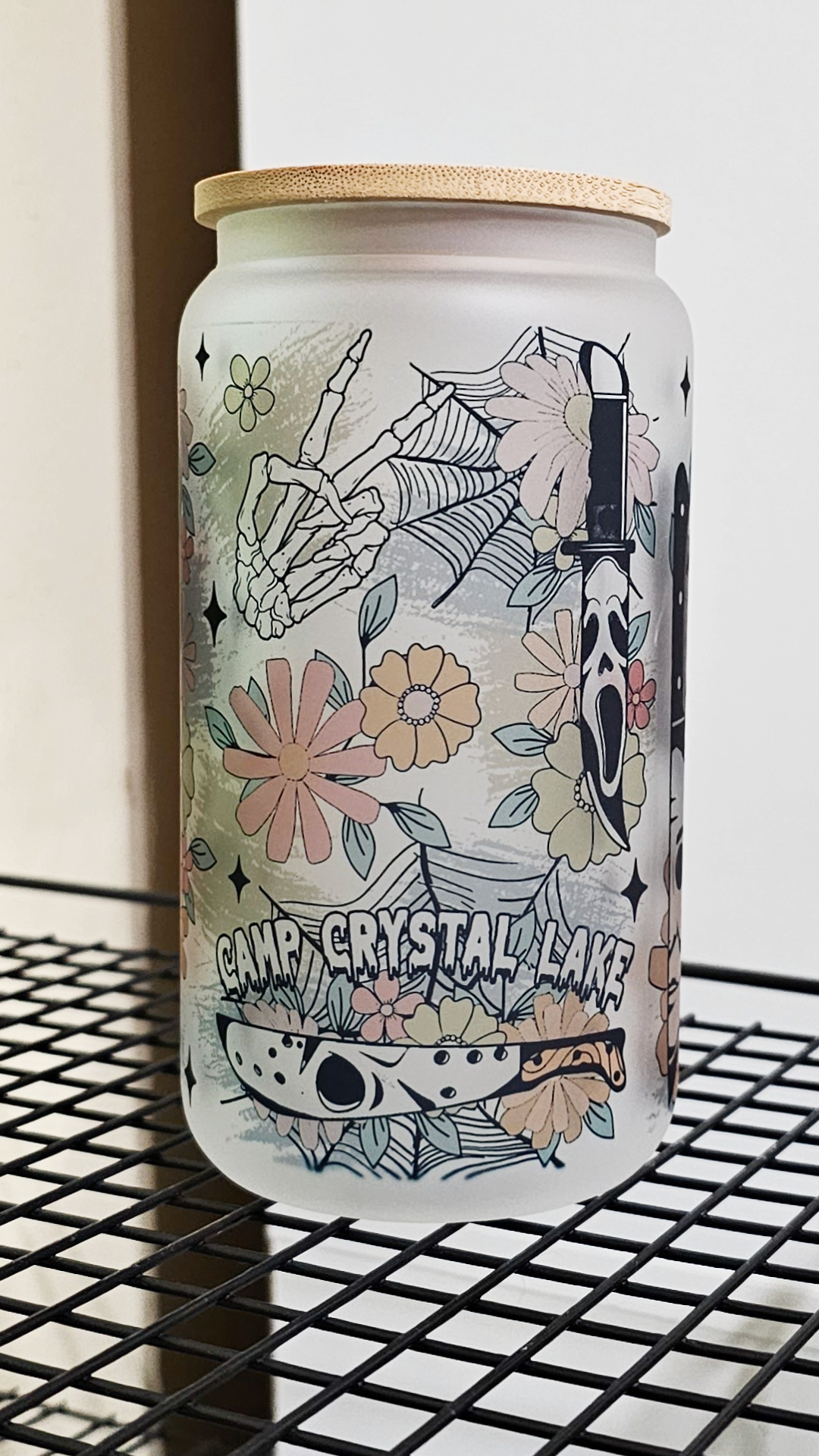 A 16oz glass tumbler featuring a blend of floral motifs and horror movie characters