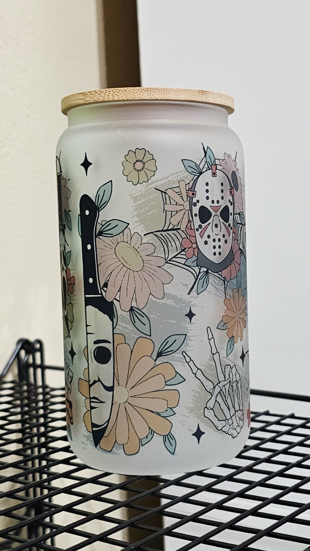 A 16oz glass tumbler featuring a blend of floral motifs and horror movie characters