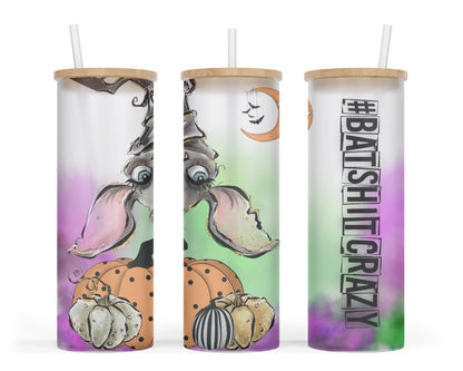 A 25oz frosted glass tumbler with a Halloween-themed design featuring a bat hanging upside down from a tree, pumpkins on the ground, and the words '#batshitcrazy' written on it