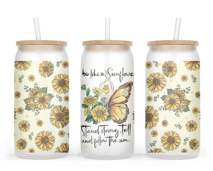 A 16oz frosted glass tumbler featuring a whimsical design of a girl with sunflower wings on one side and butterfly wings on the other, surrounded by sunflowers, with the words 'be like a Sunflower; stand tall and follow the sun