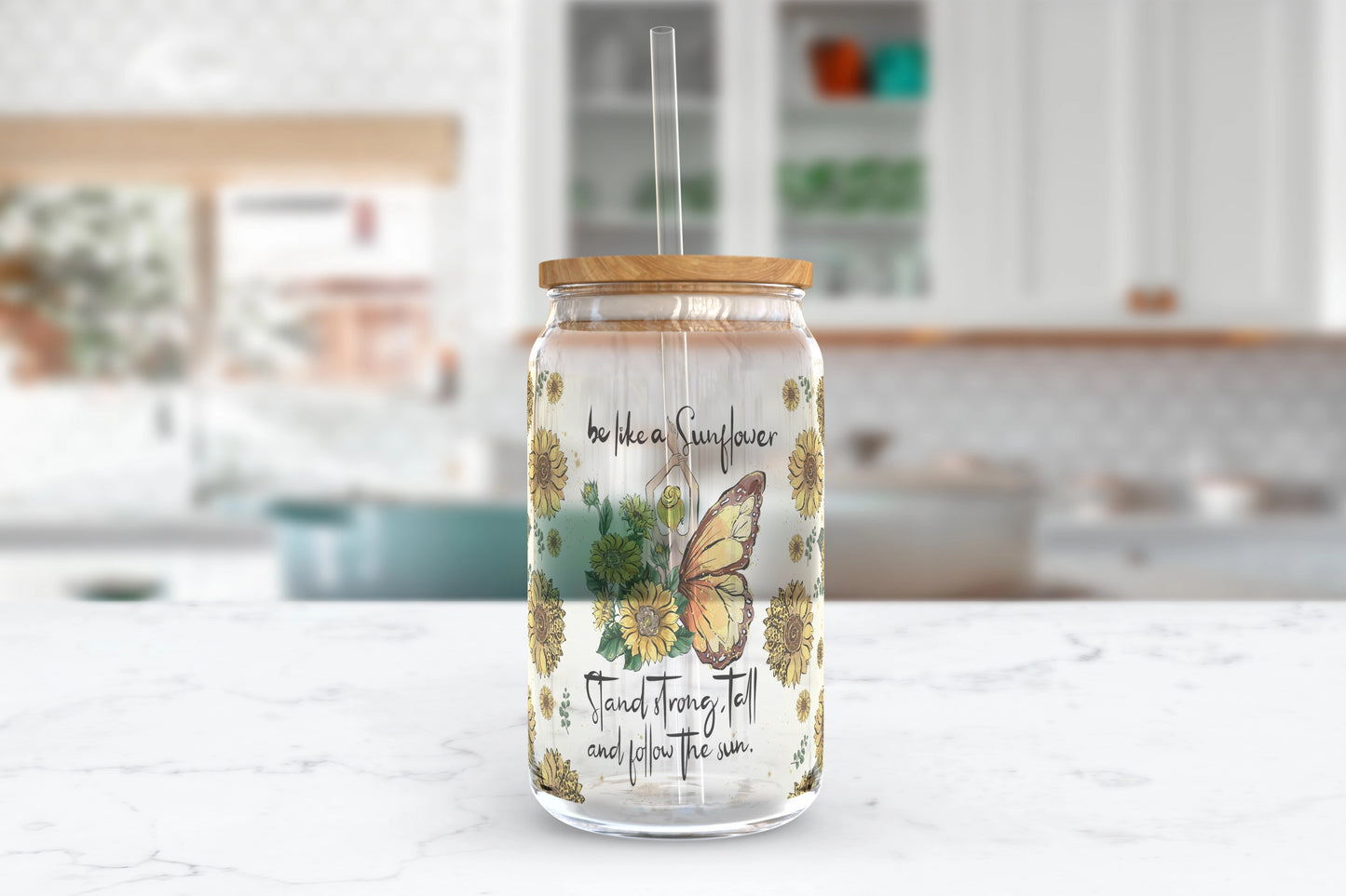 A 16oz clear glass tumbler featuring a whimsical design of a girl with sunflower wings on one side and butterfly wings on the other, surrounded by sunflowers, with the words 'be like a Sunflower; stand tall and follow the sun