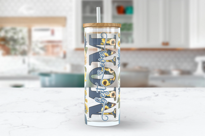 A 25oz clear glass tumbler with a blue and sunflower design. The word 'MOM' is written in bold down the side, with the words 'best ever' nested inside the letters