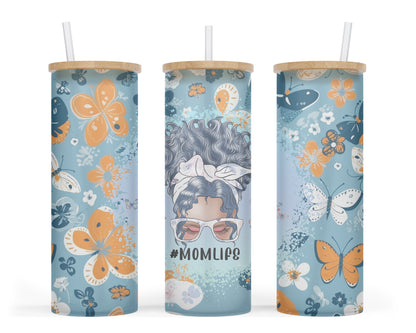 A 25oz frosted glass tumbler featuring a vibrant floral butterfly design on a blue background, with a graphic of a messy bun mom and the words '#momlife'